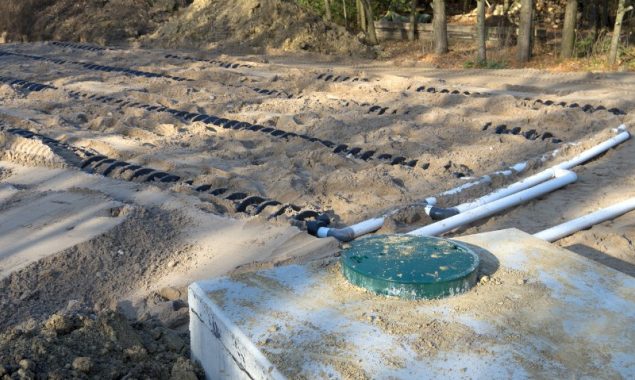 A picture of a septic tank drainage field showing the drains partially burried under sand.